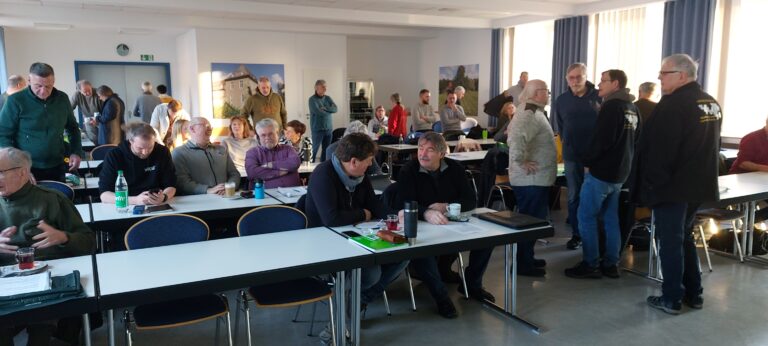 Zahlreiche Teilnehmer sitzen an Tischen in einem hellen Konferenzraum bei einer Versammlung oder Schulung.