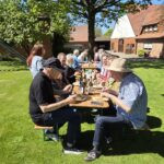 Mitglieder des Imkervereins Herford sitzen bei sonnigem Wetter an Biertischen auf einer grünen Wiese vor einem historischen Fachwerk-Bauernhof und essen gemeinsam.