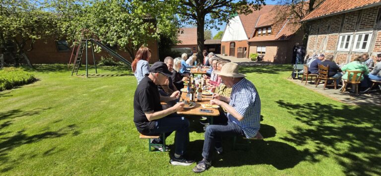 Mitglieder des Imkervereins Herford sitzen bei sonnigem Wetter an Biertischen auf einer grünen Wiese vor einem historischen Fachwerk-Bauernhof und essen gemeinsam.